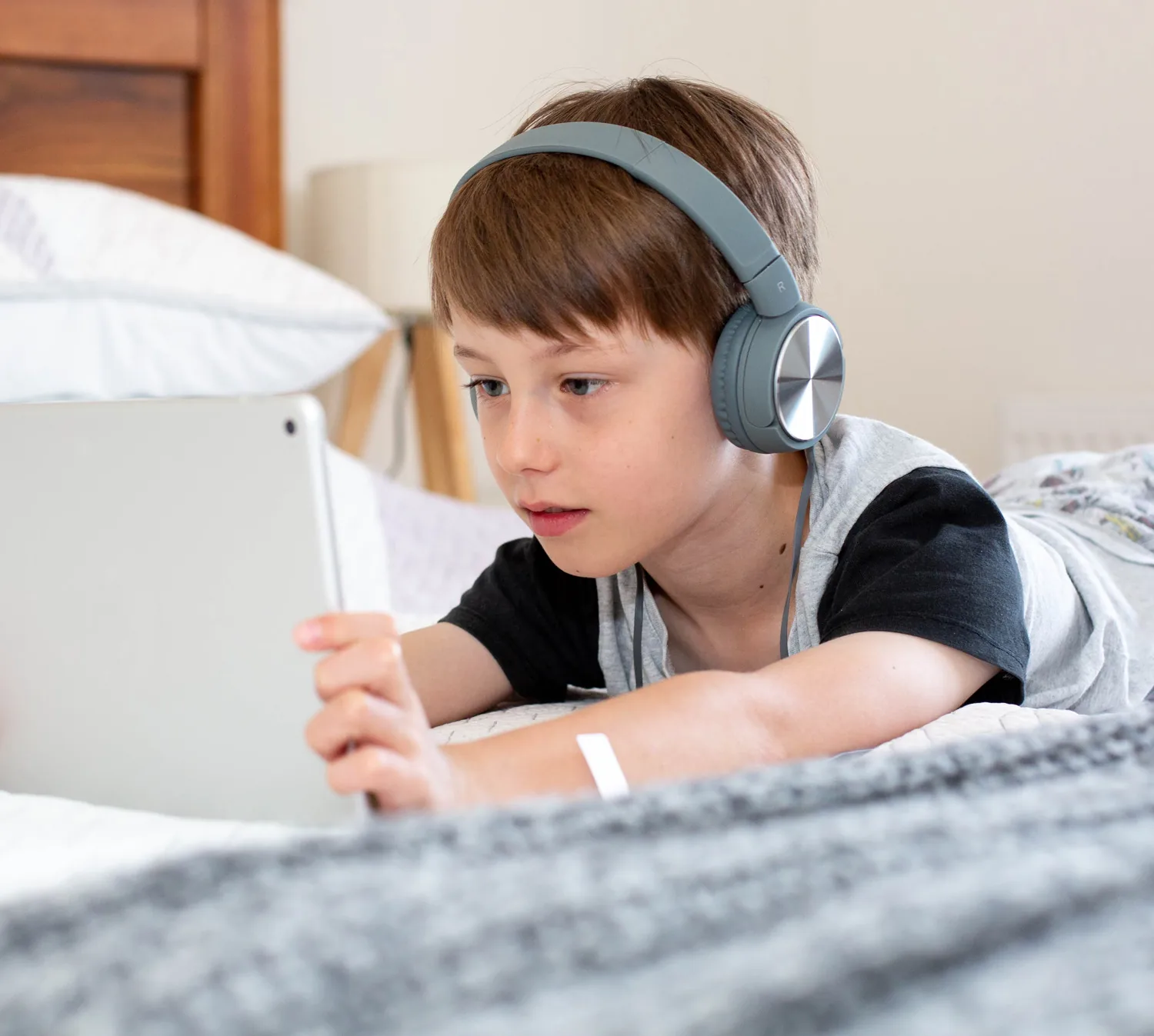 Jeune garçon avec un casque d'écoute qui regarde une tablette couché sur un lit