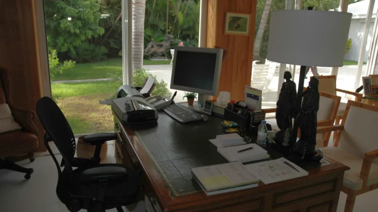 Petit bureau en bois avec un ordinateur, une lampe et une chaise devant une grande fenêtre