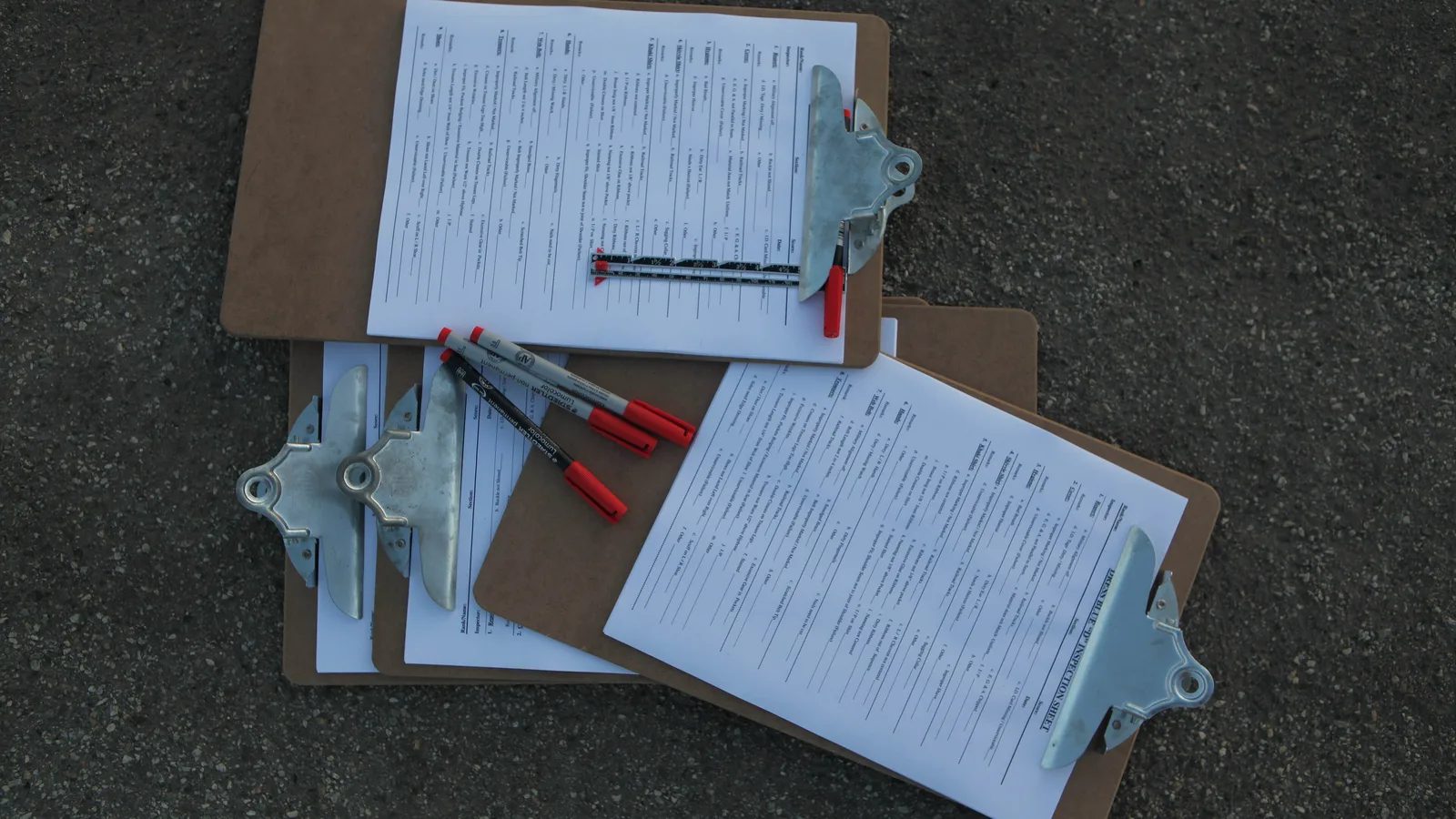 Planchettes à pince avec des formulaires de vérification et des stylos rouges posées au sol