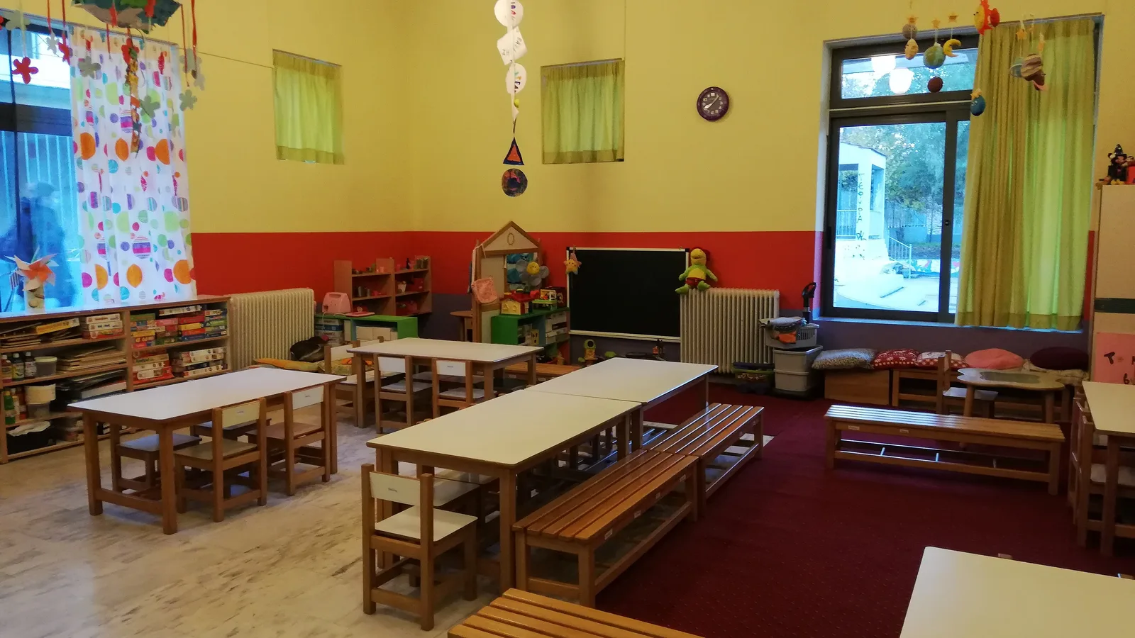 Salle de garderie vide avec petites tables en bois, bancs et murs jaunes et rouges