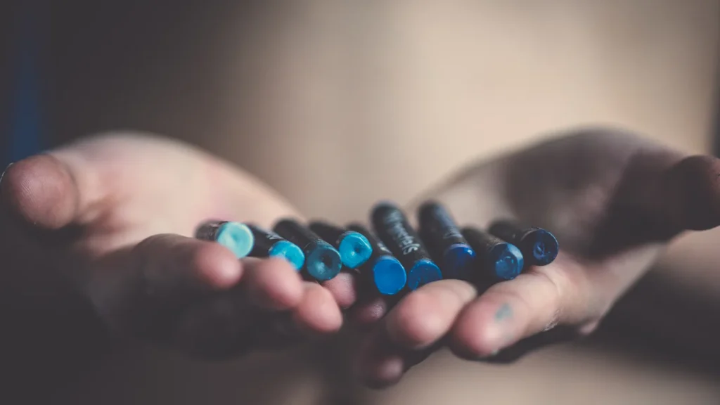 Deux mains ouvertes tenant des crayons gras dans des tons de bleu