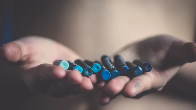 Deux mains ouvertes tenant des crayons gras dans des tons de bleu