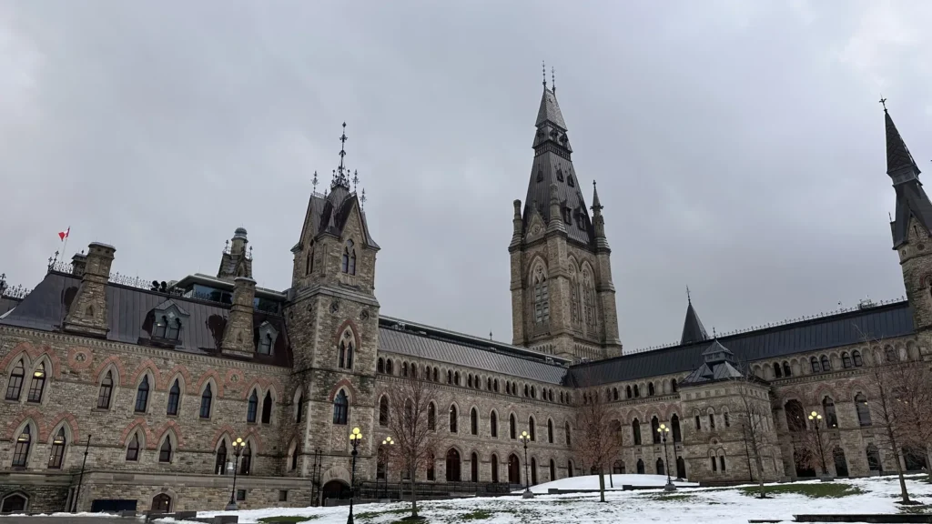 Bâtiment en pierre de la colline du Parlement à Ottawa, avec une haute tour, sous un ciel nuageux d'hiver