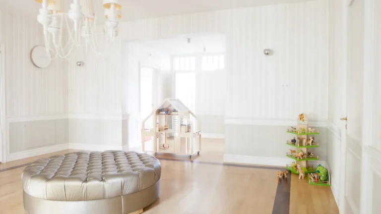 Grande salle de jeu lumineuse et vide avec un pouf rembourré, une maison de poupée en bois et des jouets rangés sur une étagère