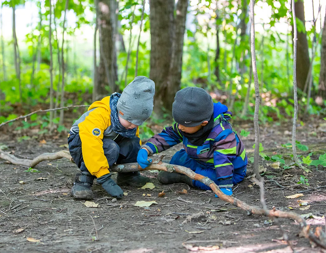 Deux jeunes enfants en manteau qui jouent avec une branche en forêt